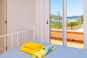 A bedroom with a bed, a window, and a view of a coastal area.