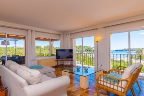 A spacious living area with a glass coffee table, a television, and a view of the sea.