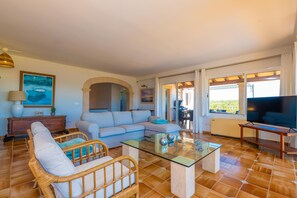 Un salon avec un canapé, des fauteuils, une table basse en verre, un téléviseur et une vue par la fenêtre.