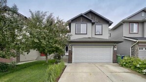 A two-story house with a garage, a well-maintained lawn, and mature trees. - Charming 1BR Basement Suite w Parking Calgary (Calgary)