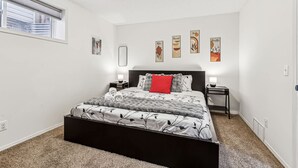 A bedroom with a bed, bedside tables, wall art, and a window. - Charming 1BR Basement Suite w Parking Calgary (Calgary)