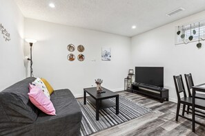 A modern living room with a grey sofa, black coffee table, and a TV stand. - Charming 1BR Basement Suite w Parking Calgary (Calgary)