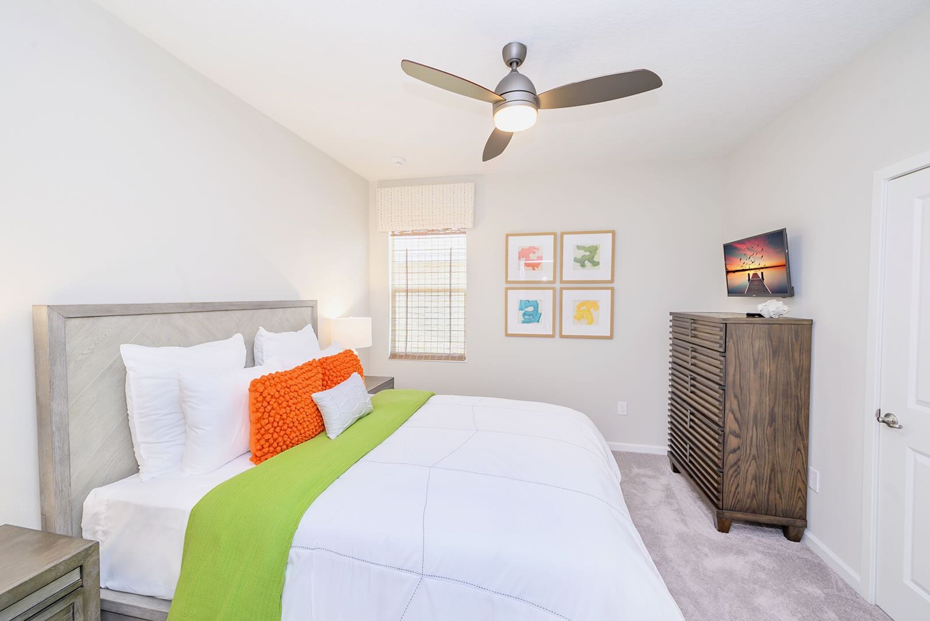 Een slaapkamer met een bed, een plafondventilator, een dressoir en ingekaderde foto's aan de muur.