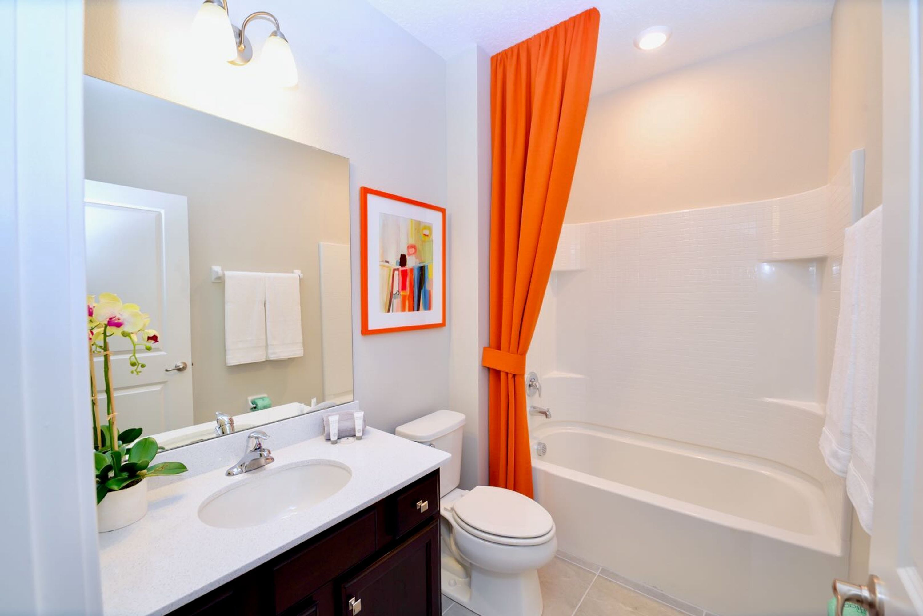 Een badkamer met een witte wastafel, spiegel en toilet, een bad en een oranje douchegordijn.