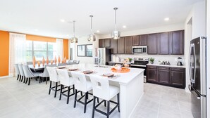 A modern kitchen with dark cabinets, a central island, and a dining area with white chairs.