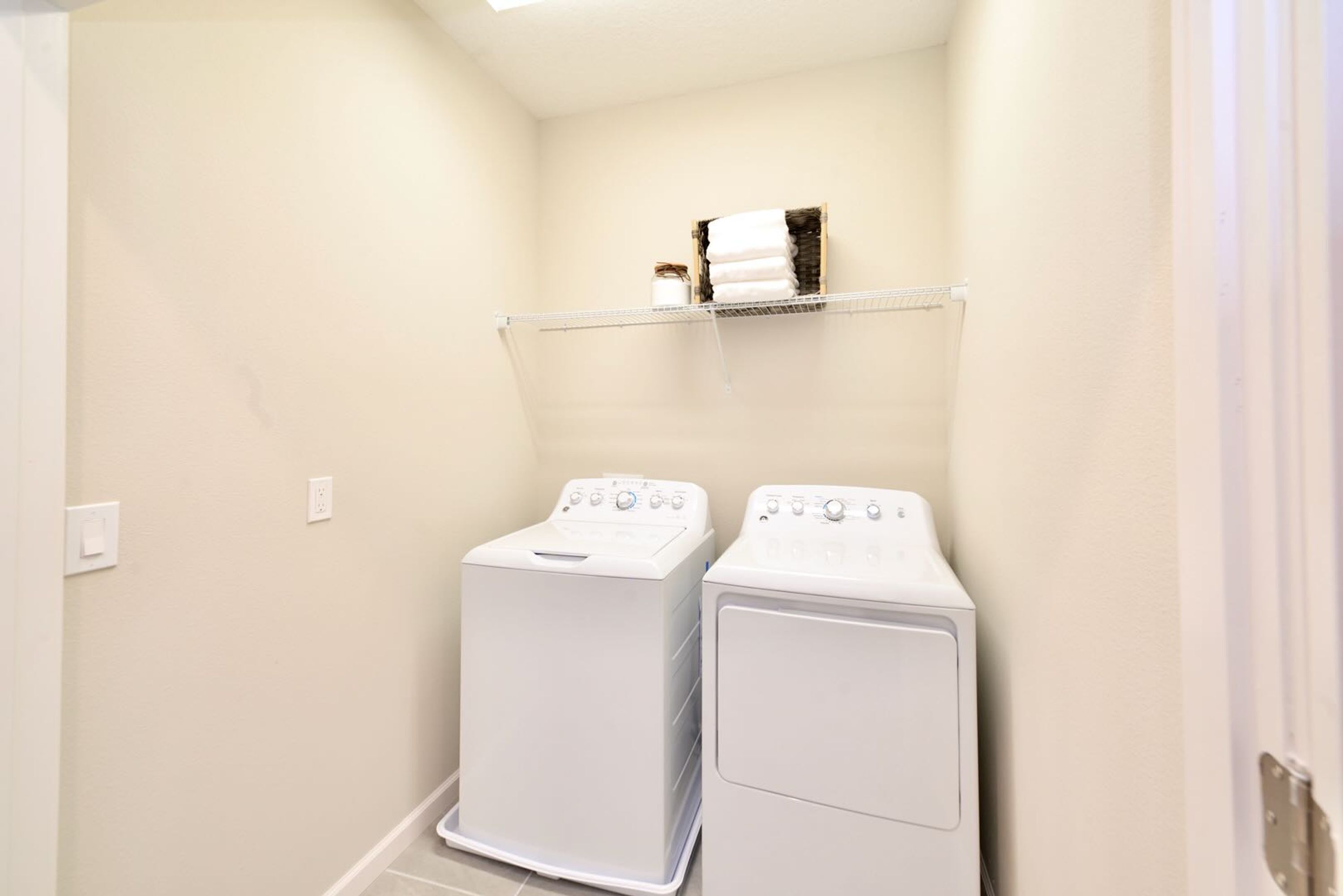 A laundry room with two white washing machines and a shelf above them.