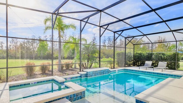 A swimming pool with a glass enclosure, surrounded by lounge chairs and a view of greenery.