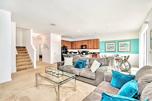 A modern living room with a glass coffee table, a grey sofa with blue cushions, and a staircase leading to another room. - Upstay Lakefront Home w Pool Cinema Games BBQ (Kissimmee)