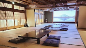 A tatami mat room with a long table and cushions, a sliding door, and a view of a mountain. - Suzukagojo (Nagahama)