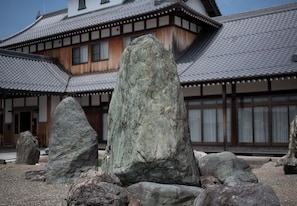 A traditional Japanese building with a tiled roof and wooden walls, surrounded by large rocks. - Suzukagojo (Nagahama)