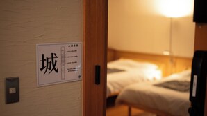 A hotel room with a bed, a bedside table, and a wall-mounted sign with Japanese text. - Suzukagojo (Nagahama)