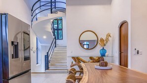 Eine moderne Küche mit integriertem Kühlschrank, einem Holztisch mit Vase und einem Spiegel an der Wand, sowie einer Treppe zu einer oberen Ebene.
