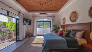 Ein Schlafzimmer mit einem großen Bett, einem Deckenventilator, einem Fernseher und Blick ins Freie.