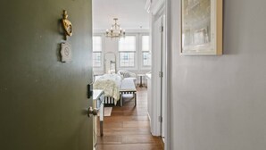 A hallway leading to a bedroom with a bed, bench, and a chandelier. - Condo Studio/Pool/StepsTO Beach/DINE (Palm Beach)