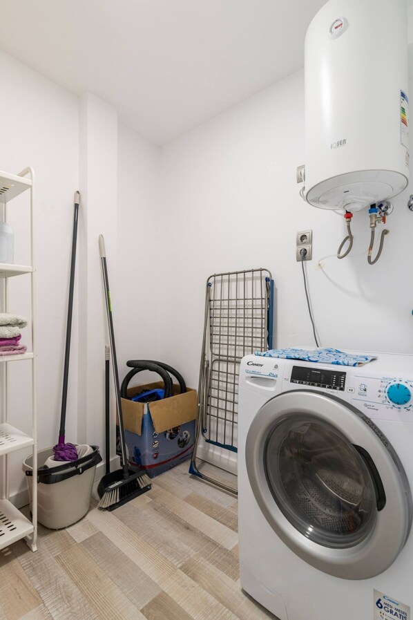 A laundry room with a washing machine, a mop, a broom, a laundry basket, and a radiator.