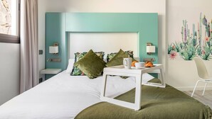 Quarto de hotel moderno com uma cama, uma mesinha de cabeceira, uma cadeira e um mural na parede.