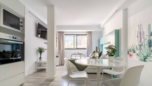 Uma cozinha moderna com eletrodomésticos embutidos, sala de jantar com mesa redonda e cadeiras brancas, e uma janela grande com cortinas.