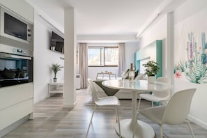 Una cocina moderna con electrodomésticos integrados, un comedor con una mesa redonda y sillas blancas, y un ventanal con cortinas.