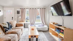 En moderne stue med sofa, sofabord i træ, bænkbænk i sten, tv ophængt på væggen og et bogreol.