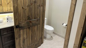 A bathroom with a wooden vanity, a toilet, and a white sink.