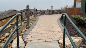 A stone pathway leading to a building with a wooden fence and metal railings.