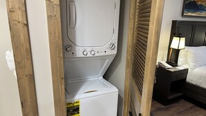 A compact washer and dryer unit with control knobs, a price tag, and a wooden door frame.