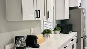A modern kitchen with white cabinets, a black coffee maker, a microwave, and a stainless steel refrigerator.