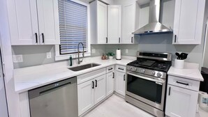 A modern kitchen with white cabinets, stainless steel appliances, a dishwasher, and a window with blinds.