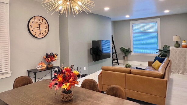 A modern living room with a dining area, featuring a chandelier, a clock, a sofa, and a television.