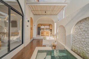 Ein modernes Interieur mit Steinwand, Holzboden, Schwimmbecken und Küchenbereich.