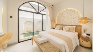 Camera da letto con un grande letto, una panca, vista su una piscina a sfioro e un muro in pietra.