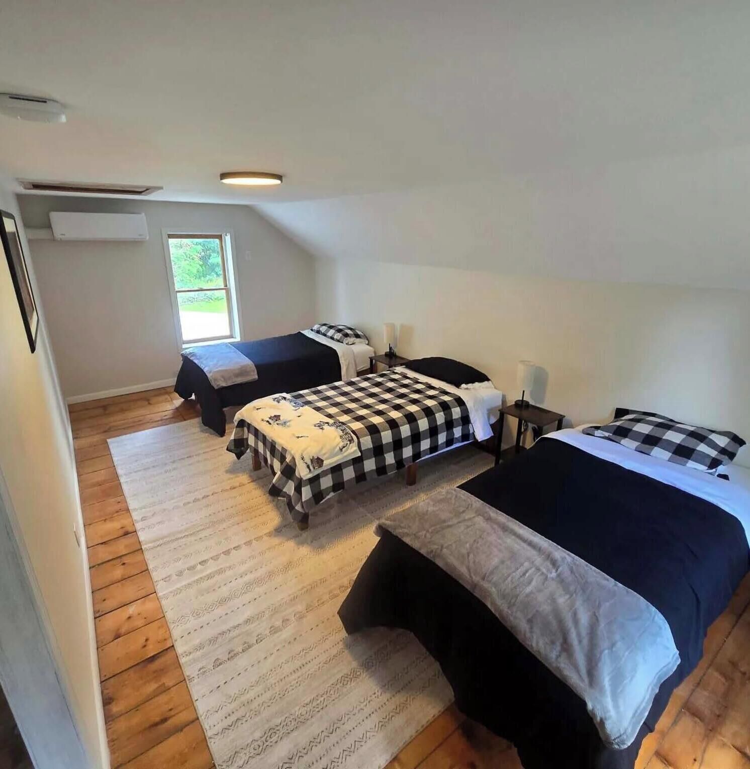 Ein Zimmer mit zwei Betten, Holzboden, einem Fenster und einer Deckenleuchte.