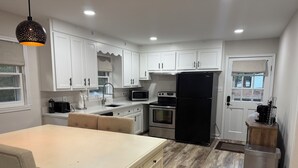 A modern kitchen with white cabinets, a black refrigerator, stainless steel appliances, and a wooden floor. - Cozy 3-bedroom house with AC in charming Waxhaw (Waxhaw)