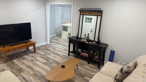 A living room with a flat-screen TV on a wooden stand, a small wooden table, a sofa with patterned cushions, a console table with decorative items, and a large mirror. - Cozy 3-bedroom house with AC in charming Waxhaw (Waxhaw)