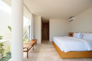 Quarto moderno com cama grande, um banco de madeira e vista para uma varanda com plantas.