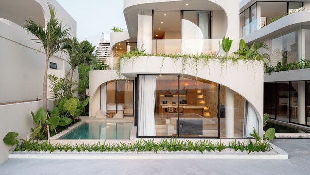 Un moderno edificio residencial de varios pisos con diseño curvo, piscina y abundante vegetación.