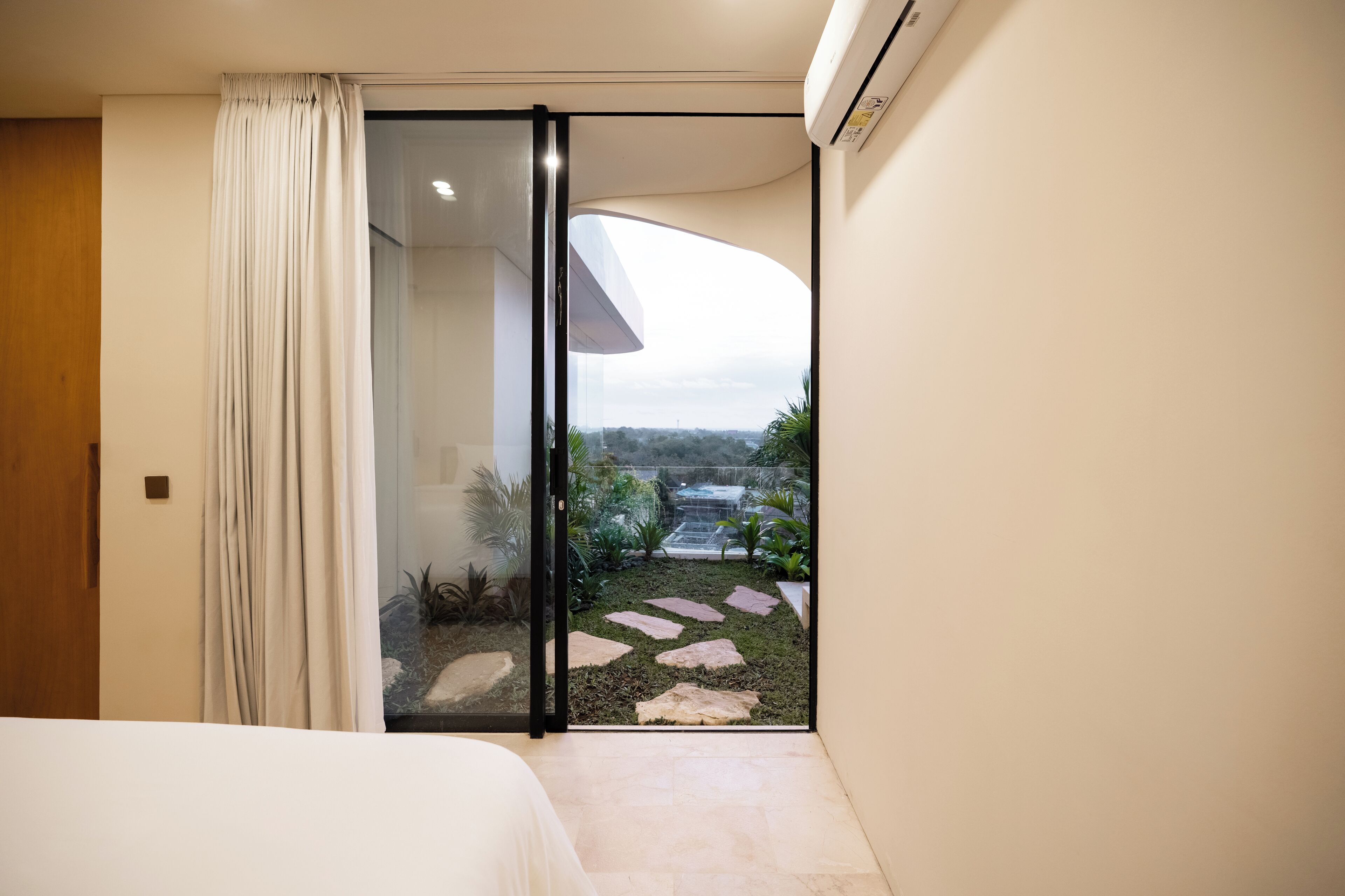 Un dormitorio moderno con un ventanal corredero que da a un balcón con vistas a un jardín.