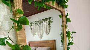 Quarto com estrutura de cama de madeira, duas almofadas e um painel de parede em macramé.