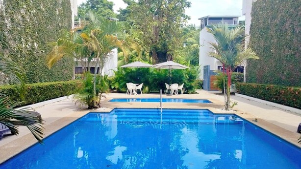 Piscina com escadas de acesso, rodeada por vegetação e um edifício branco.