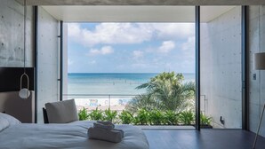 A modern hotel room with a large window offering a view of the beach and ocean. - CELEVI Yomitan (Yomitan)