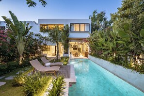 Et moderne hus med swimmingpool, omgivet af frodigt grønt og en velplejet have.