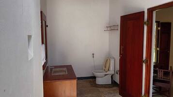 A small, compact bathroom with a toilet, a wooden cabinet, and a shower area.