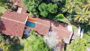 Vista aérea de una casa con techo de tejas rojas, piscina y vegetación circundante.