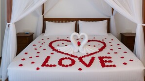 Una cama con dosel, ropa de cama blanca y una decoración con forma de corazón hecha de pétalos de rosa y cisnes.