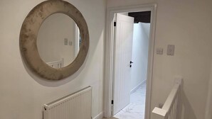 Um corredor com um radiador branco, um espelho redondo e uma porta que dá para outro quarto.