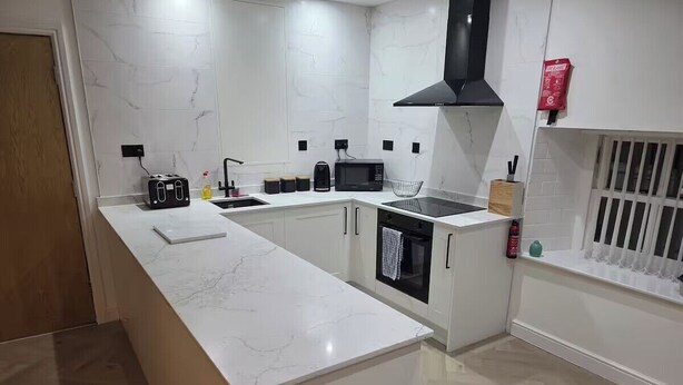 Cozinha moderna com bancada de mármore, forno embutido, micro-ondas e coifa preta.