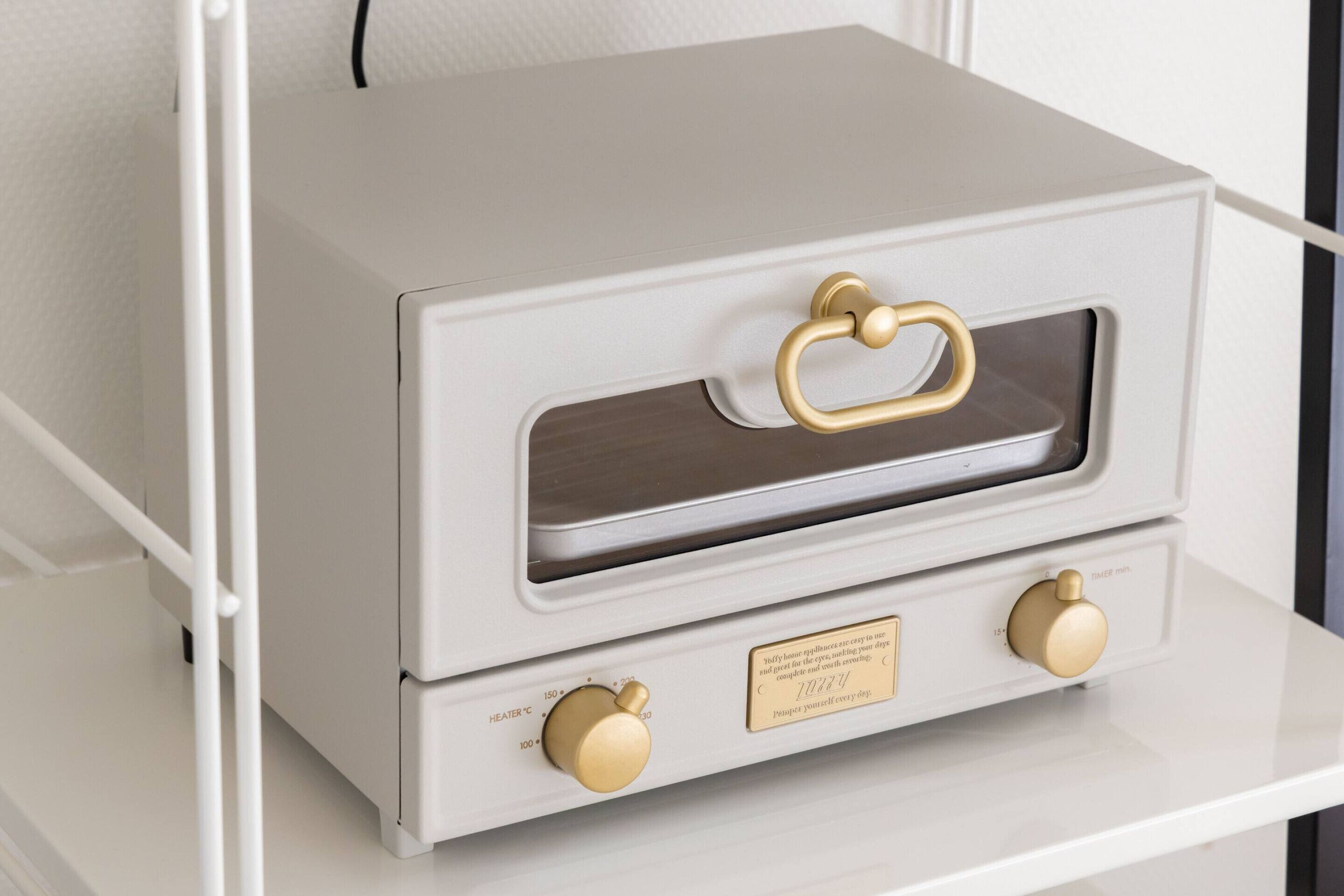 A white, two-door oven with brass handles and knobs, featuring temperature settings and a label.