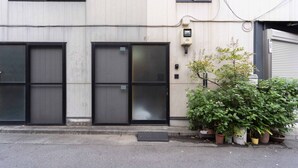 A building with three large black doors, a small potted plant, and a utility box on the wall. - House Hotel nakano TNA (Tokyo)