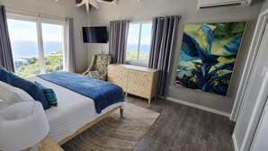 A bedroom with a bed, a dresser, a TV, and a large window with a view.
