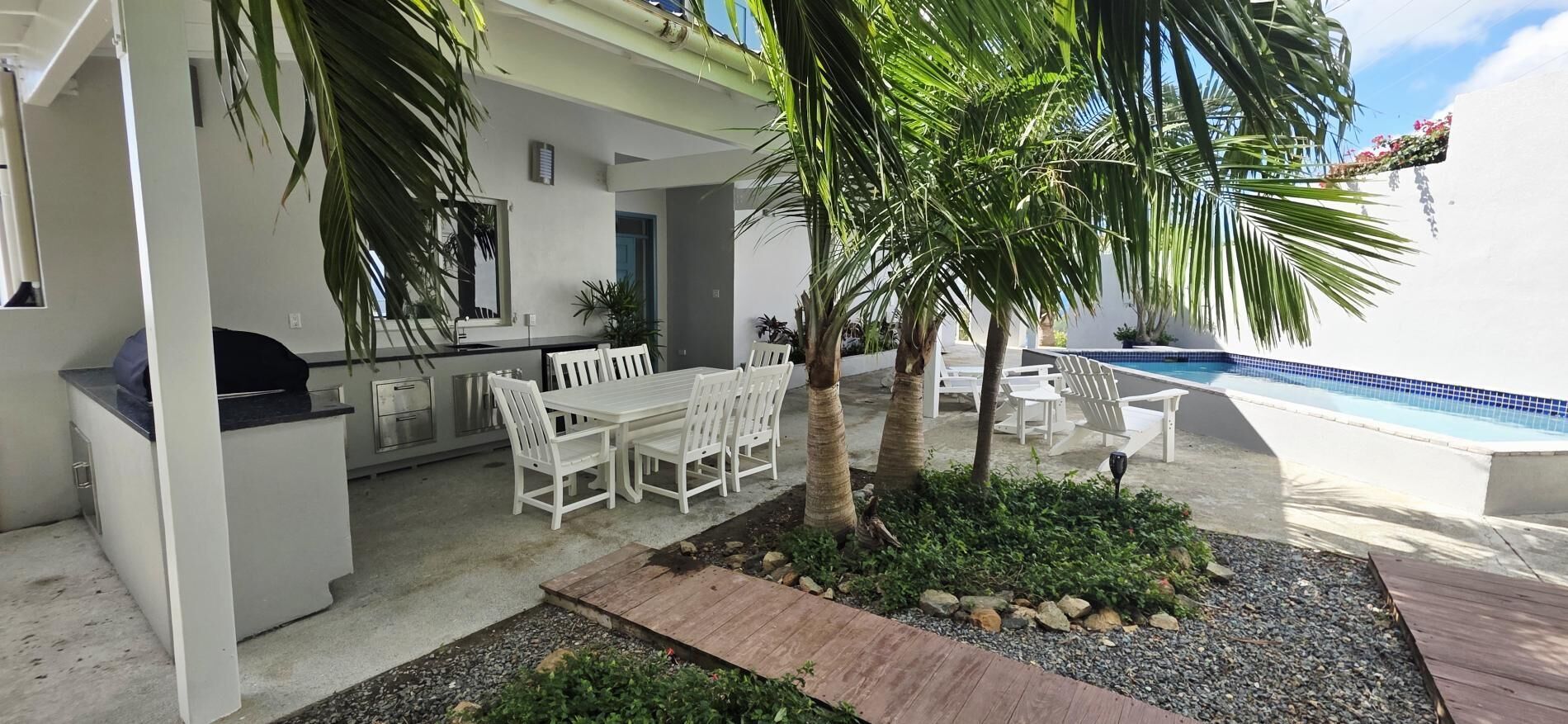 A patio with a dining table and chairs, a small pool, and palm trees.